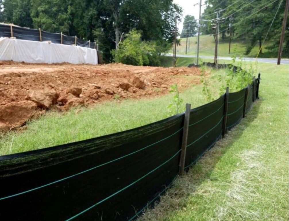Black silt fence installed on grass to prevent sediment runoff from a dirt construction site.