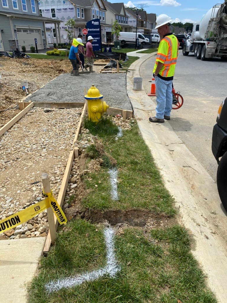 Construction workers install a new sidewalk in a residential neighborhood near a yellow fire hydrant.