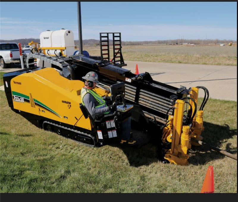 Worker in safety gear operates a yellow Vermeer horizontal directional drill on grass.