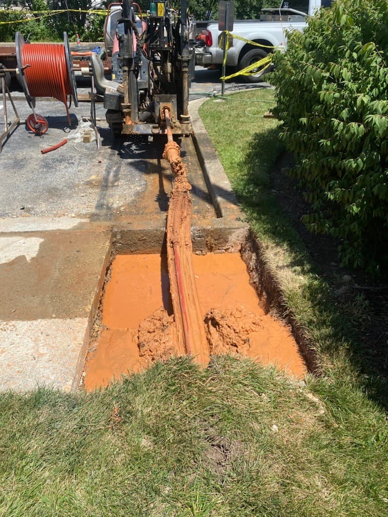 Horizontal directional drilling machine pulling a pipe through a muddy pit for underground utility installation.